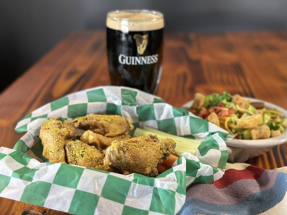 Seasoned fried chicken pieces in a checkered paper-lined basket with a pint of Guinness behind