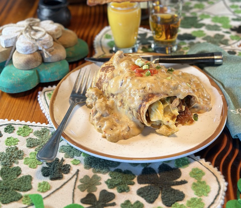 A filled roll smothered in sauce on a shamrock placemat, with orange juice and a beer