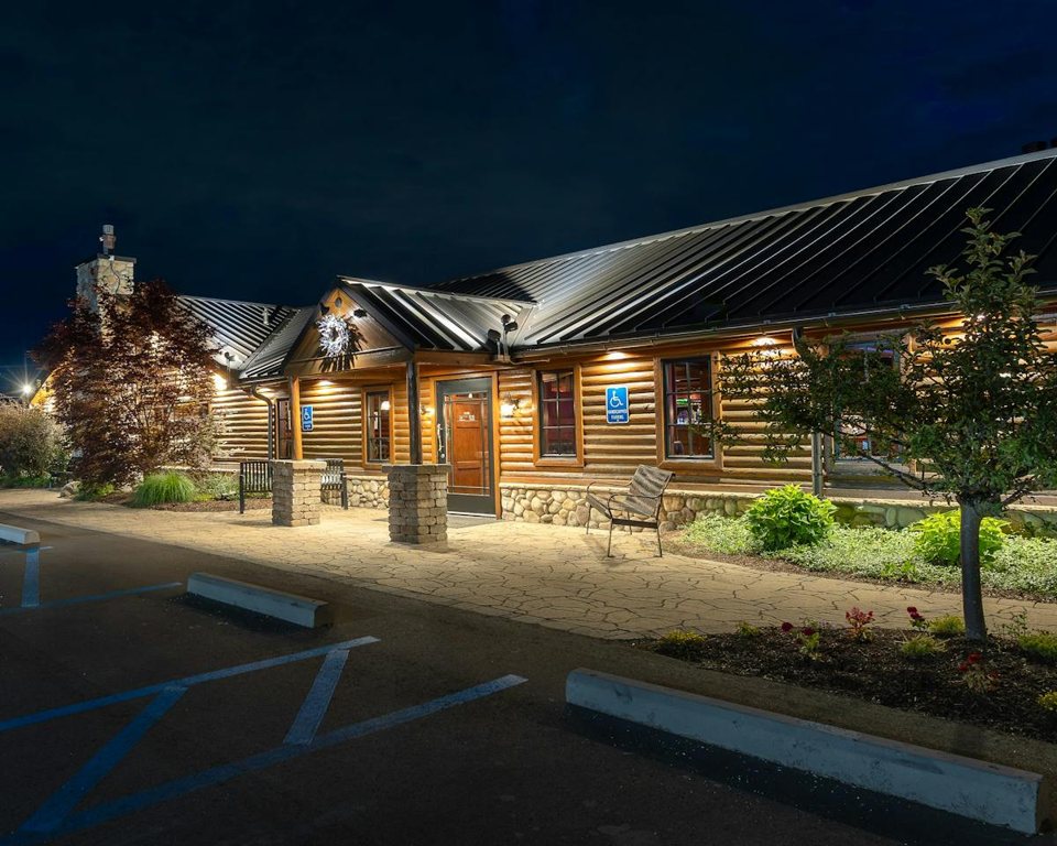 The log cabin restaurant lit up at night, with a stone walkway and flower beds in front
