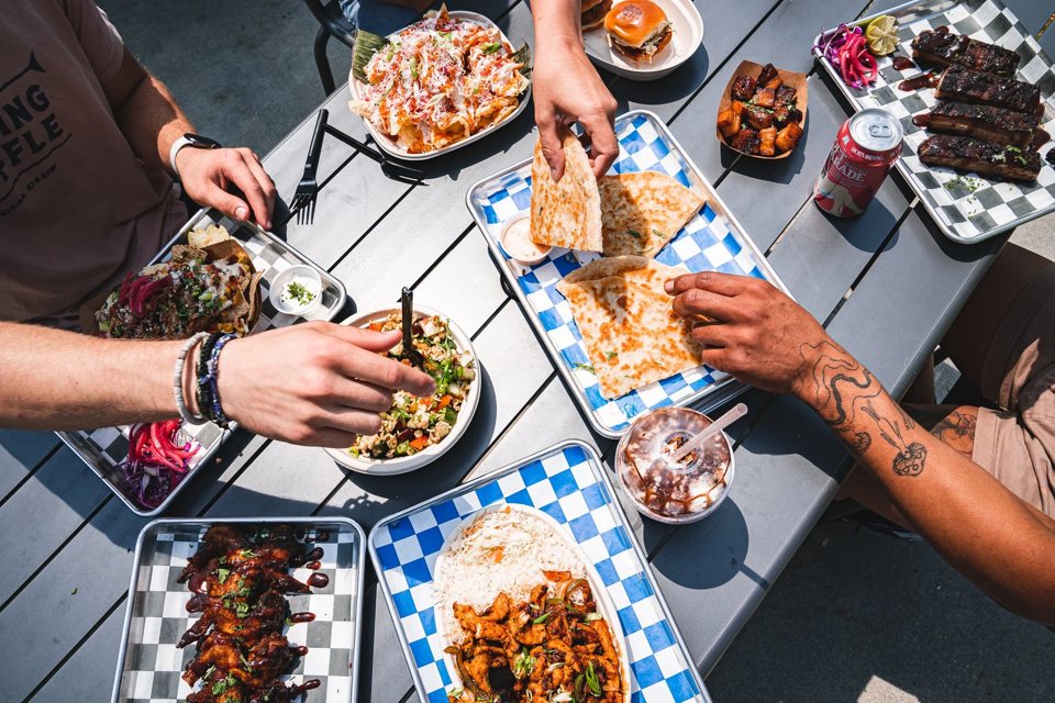 Several people sharing tacos, wings and other dishes at an outdoor table