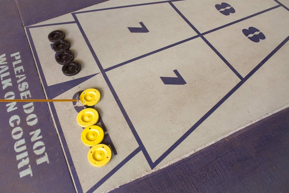 A close-up of a shuffleboard court with numbered zones and yellow and black pucks