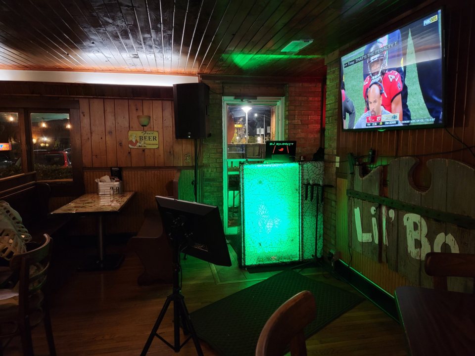A karaokesarok zölden világító DJ-pulttal, hangfalakkal, monitorral és faburkolatú falakkal