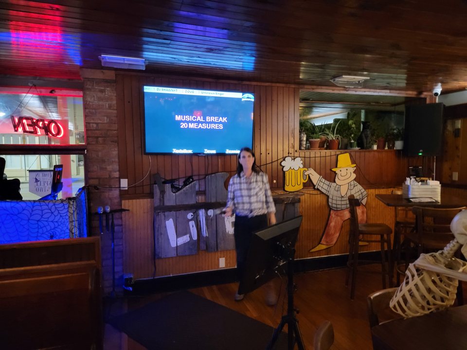 Faburkolatú bárterem, a karaokesarokban egy vendég énekel a dalszövegképernyő alatt