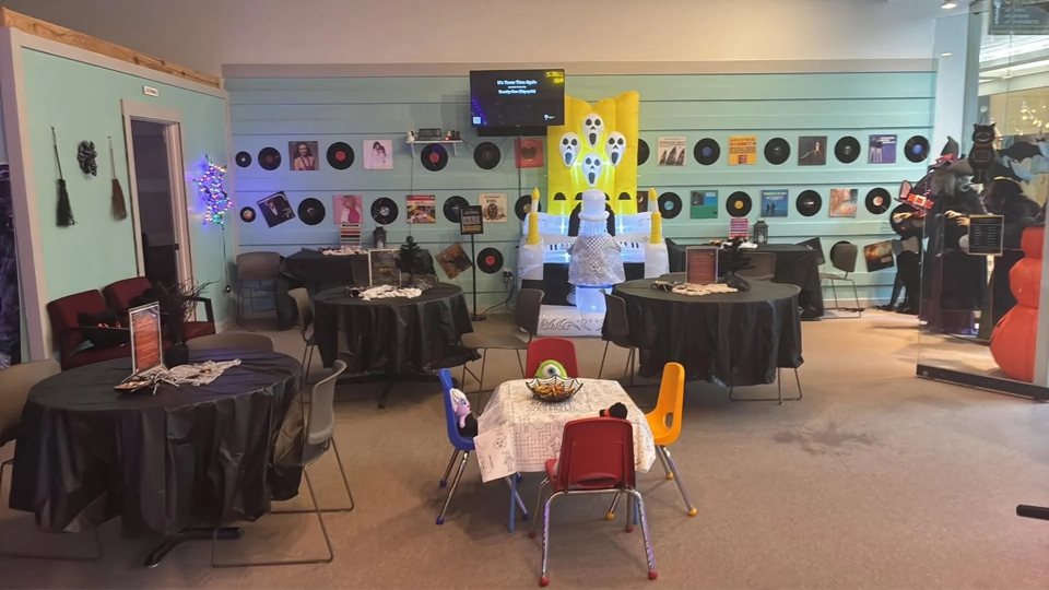 A mint-green room with round black-draped tables, kids' chairs and vinyl records on the wall