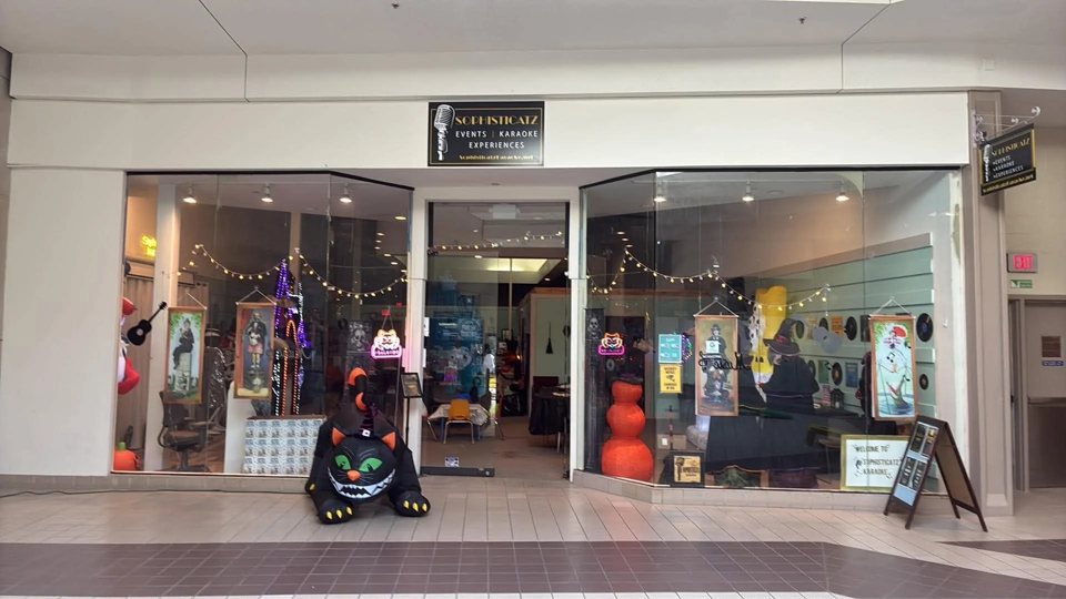 A shopping mall storefront with a Sophisticatz sign, string lights and Halloween decorations in the windows