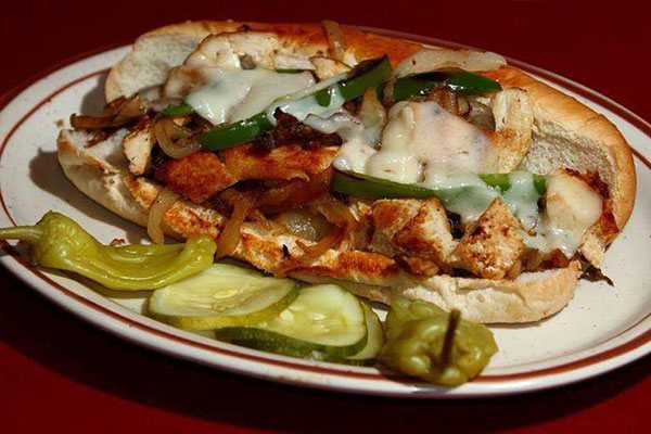A grilled chicken sandwich with peppers and cheese, pickles and pepperoncini
