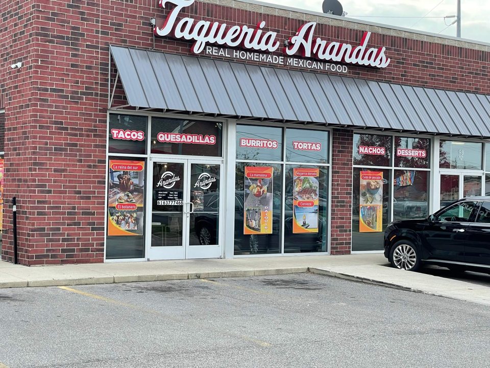 Téglaépület Taqueria Arandas felirattal, fémnapellenzővel és ételfotós plakátokkal az ablakokban