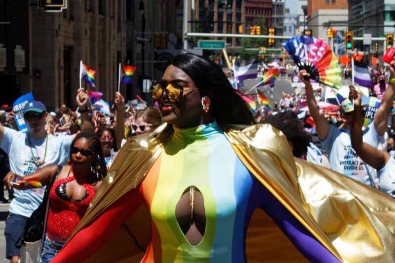 Pride-felvonulás résztvevője szivárványos ruhában és arany köpenyben