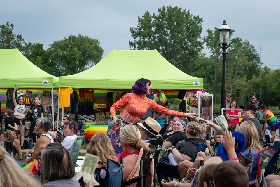 Korallszínű ruhás drag-előadó lép fel a sátrak előtt ülő közönségnek