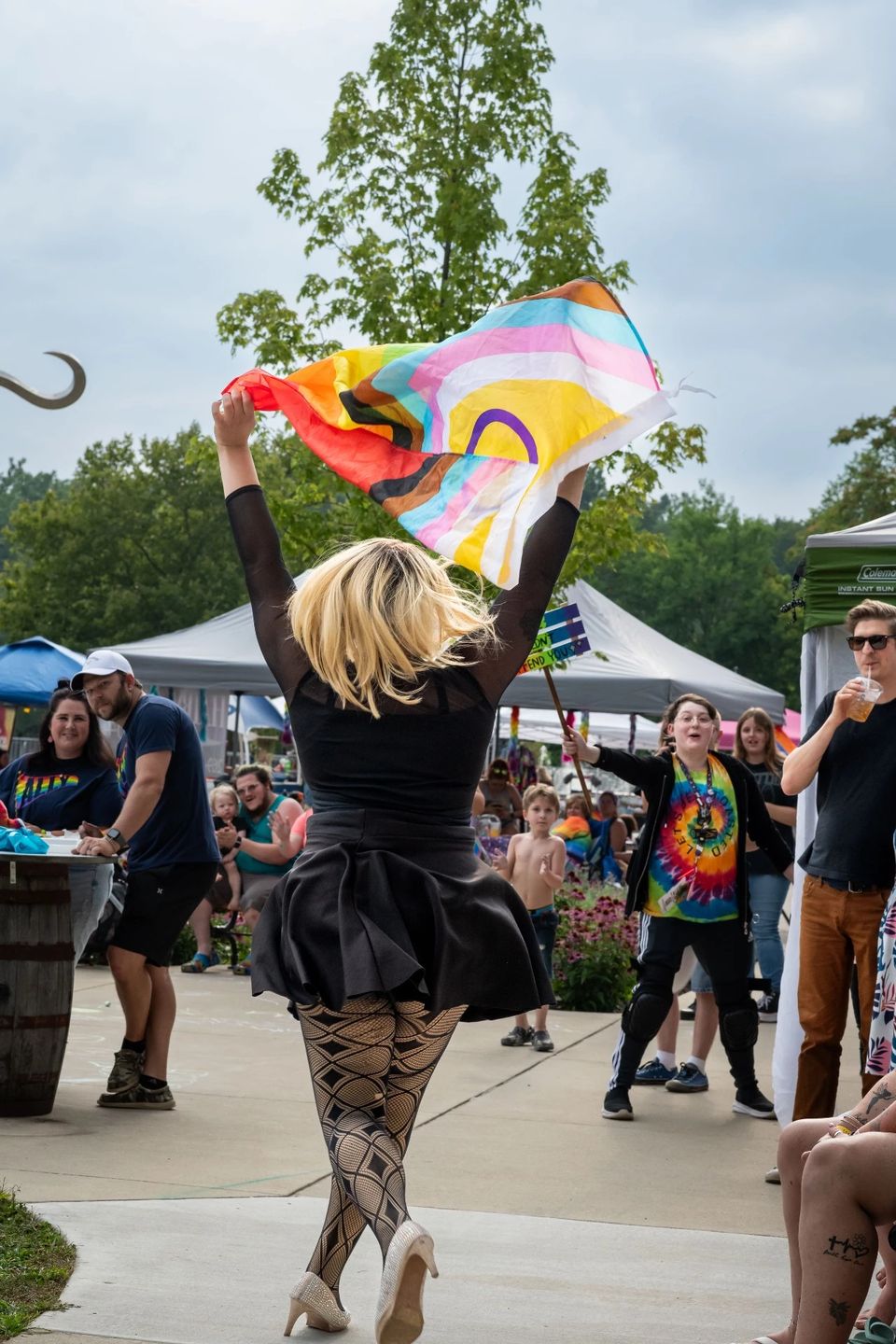 Szőke drag-előadó szivárványos zászlót lenget egy szabadtéri rendezvényen