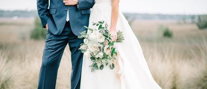 Menyasszony fehér rózsás, zöldekkel kötött csokorral a vőlegény mellett