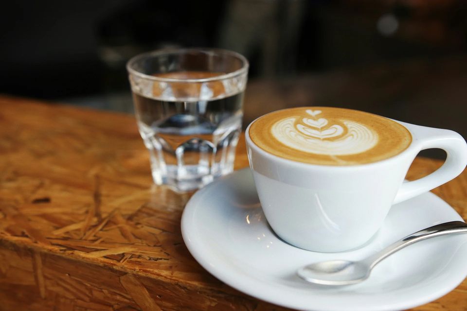 Tejeskávé latte arttal és egy pohár víz fa asztalon