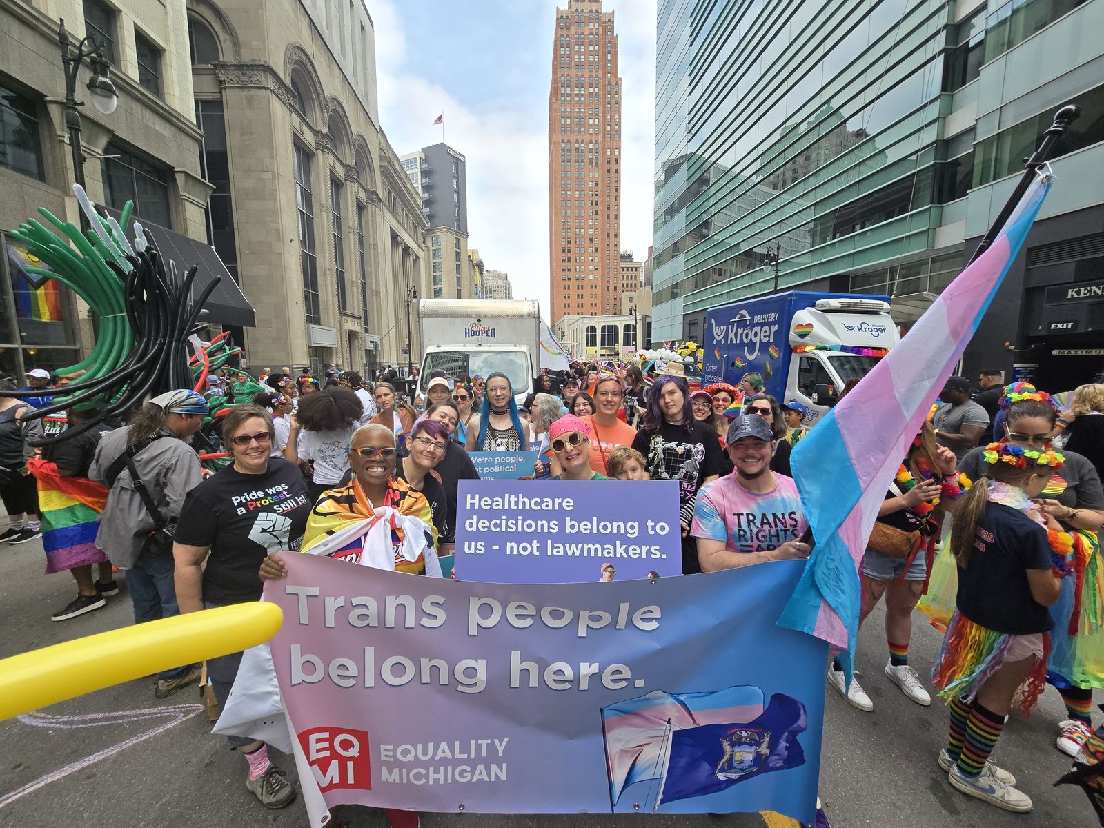Marchers with a 'Trans people belong here' banner in a downtown Pride march
