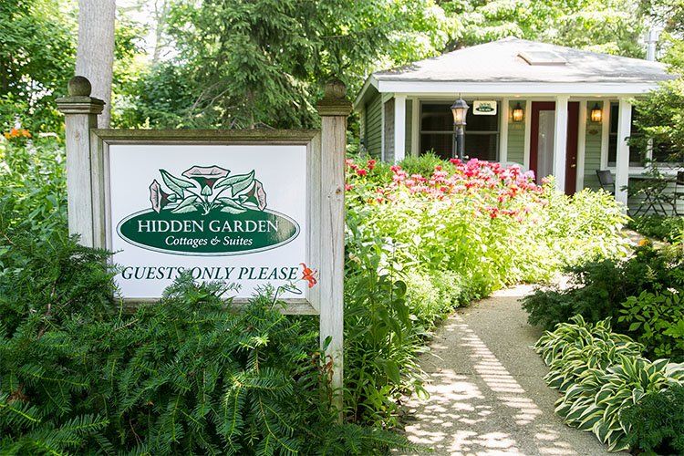 A Hidden Garden Cottages & Suites táblája a kertben, mögötte vendégház