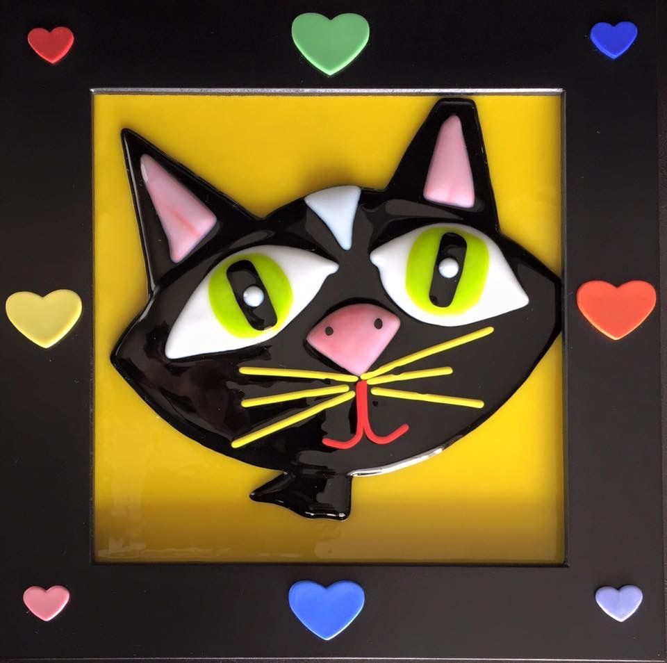 Fused-glass black cat on a yellow panel framed with colorful hearts