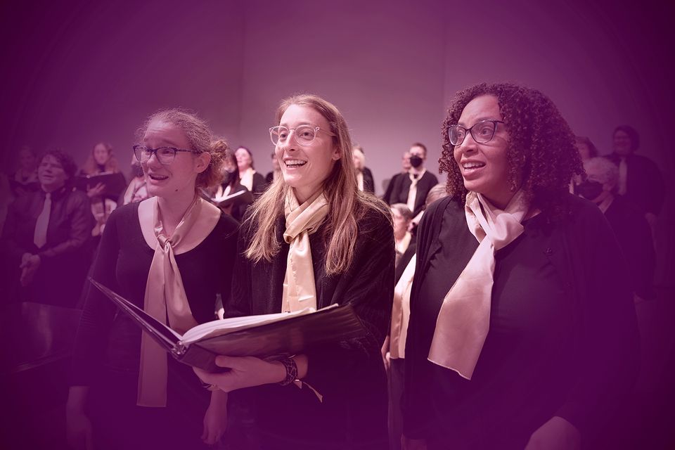Chorus members in scarves singing from music folders in purple light
