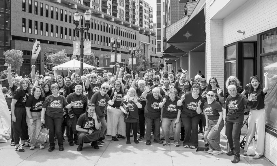Black-and-white group photo of chorus members in matching shirts on a downtown street