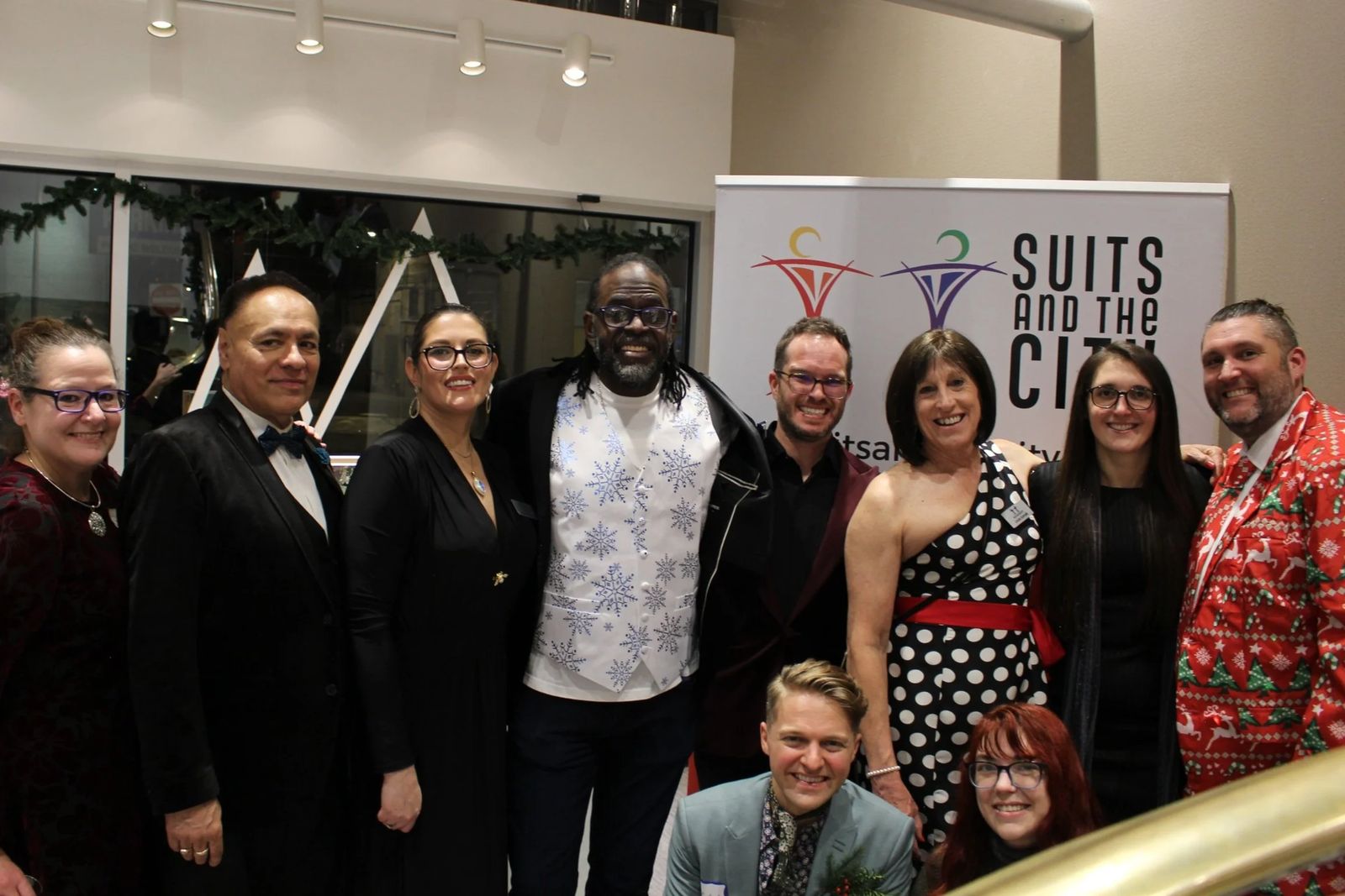 Dressed-up members pose in front of a Suits and the City banner