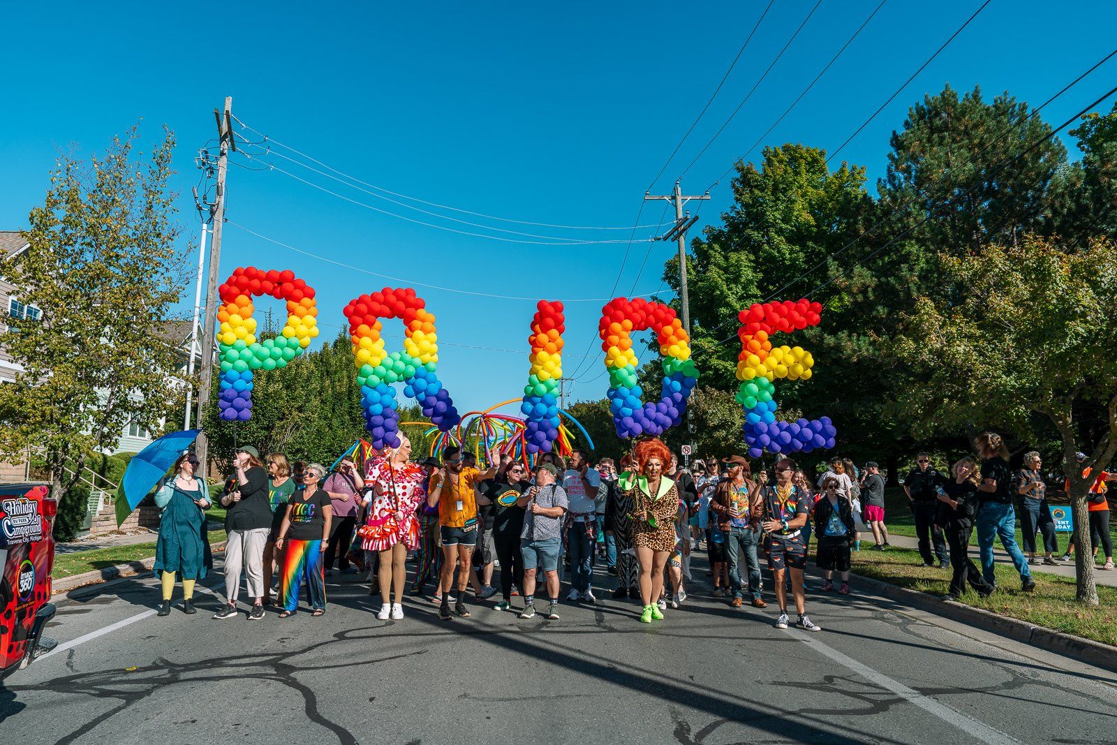 Pride-felvonulás szivárványszínű PRIDE léggömbbetűkkel egy napsütéses utcán