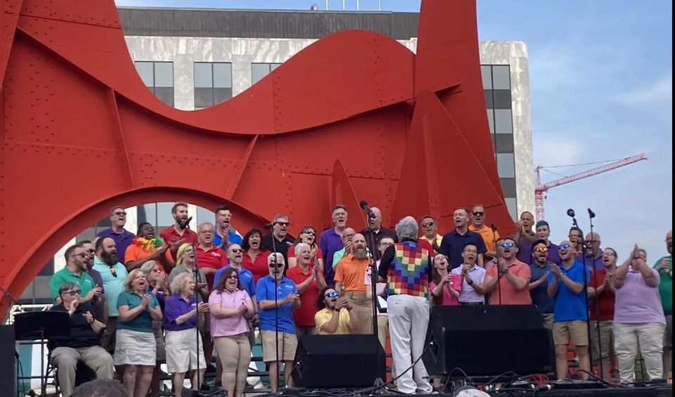 Chorus in colorful shirts performs beneath the red Calder sculpture in Grand Rapids