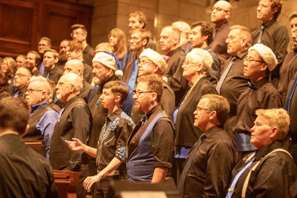 Chorus members in black shirts and blue ties singing
