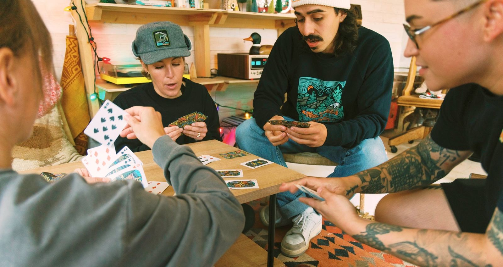 Friends play cards in a cozy room wearing Woosah-printed apparel