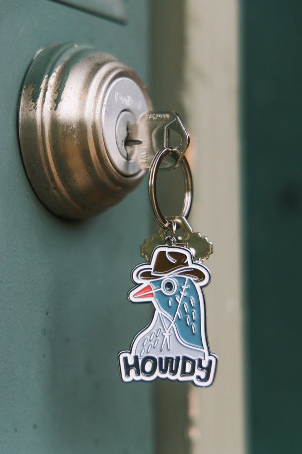 Enamel “Howdy” bird keychain hanging from a door lock