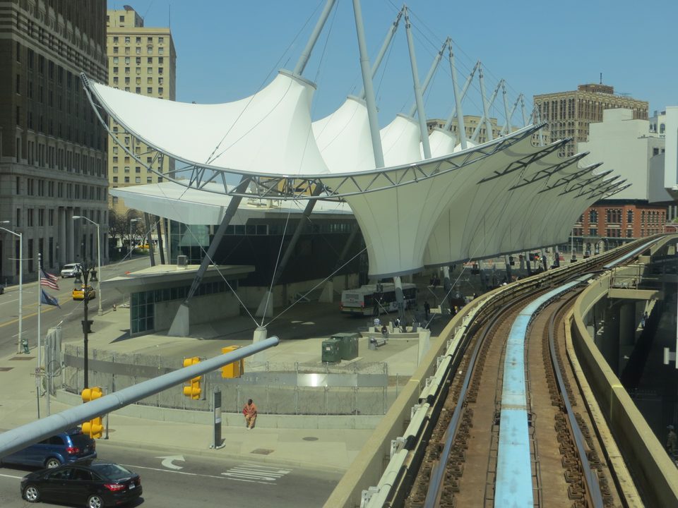 A train above Cass Avenue and Lafayette Boulevard, beside the sail roof of the Rosa Parks Transit Center (2015)