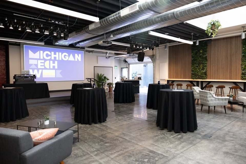 The Cahoots event room with black-draped cocktail tables, a projection screen and stage lights