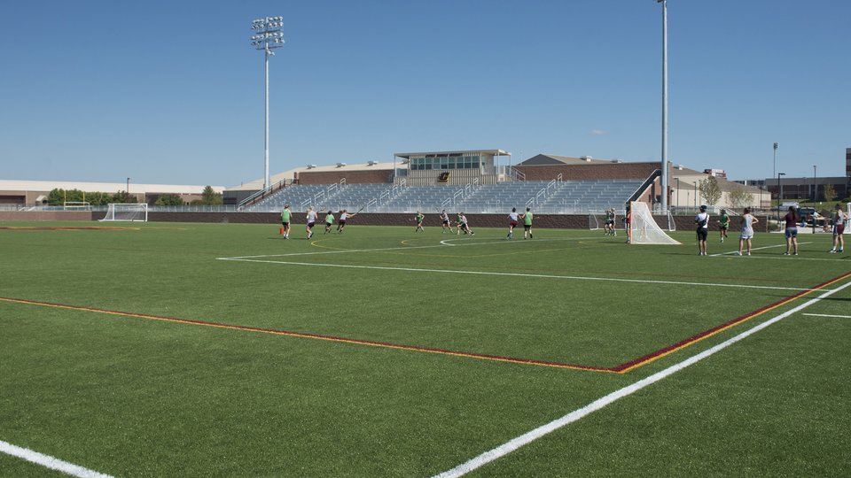 Lacrosse practice on the turf with the grandstand and press box behind