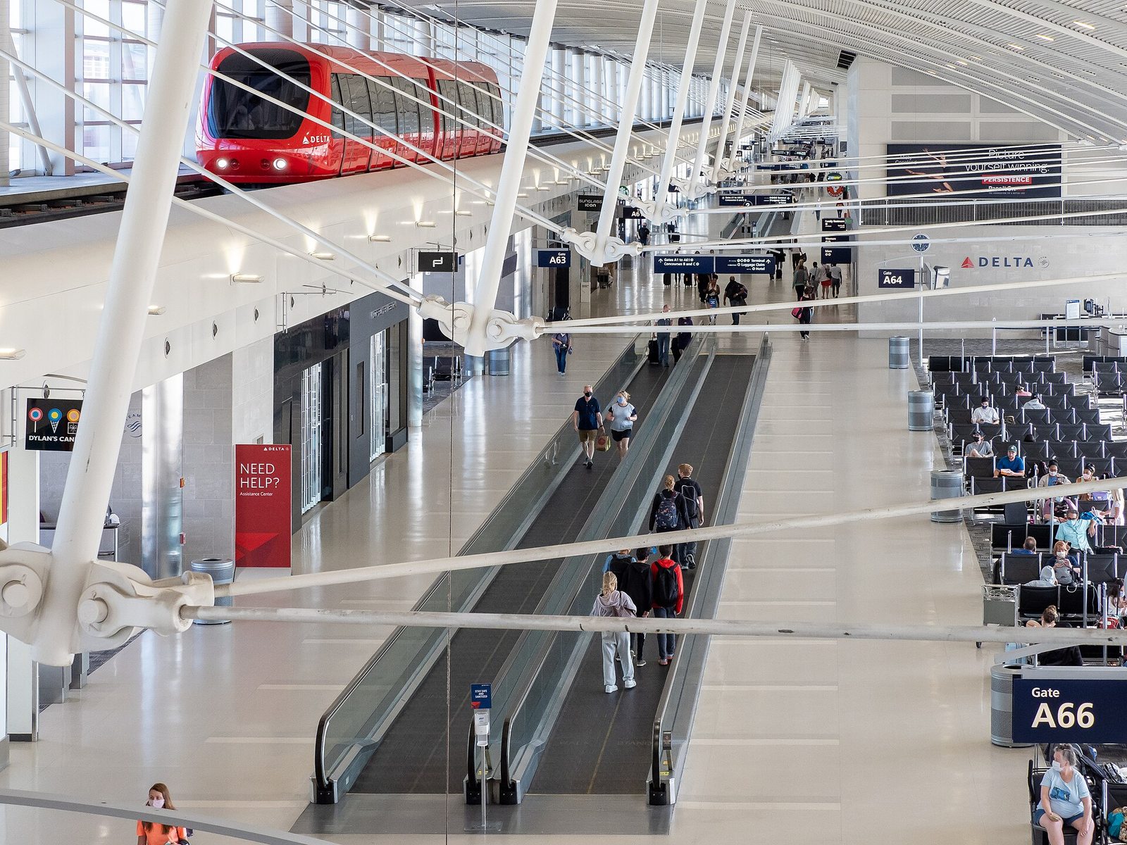 A Detroit Metro Airport McNamara termináljának világos, tágas A csarnoka: a piros ExpressTram a magasított pályán halad a mozgójárdák és a kapuknál lévő ülősorok fölött.