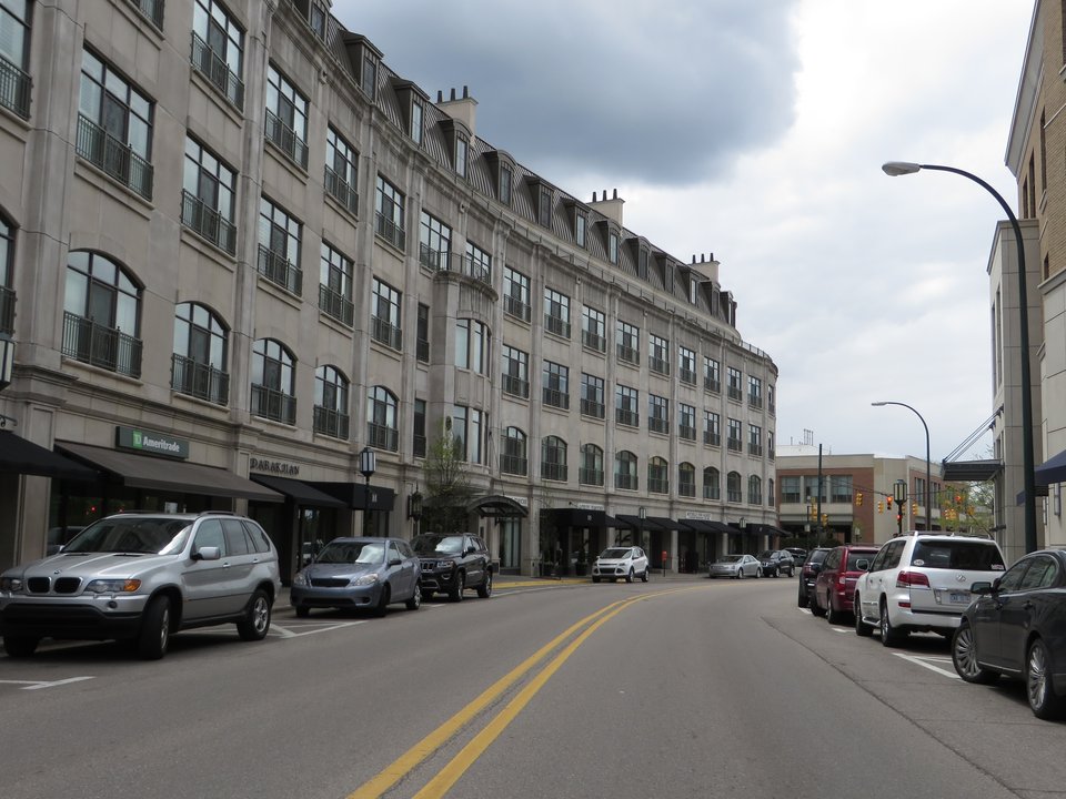 A multistory stone building with ground-floor shops and parked cars downtown