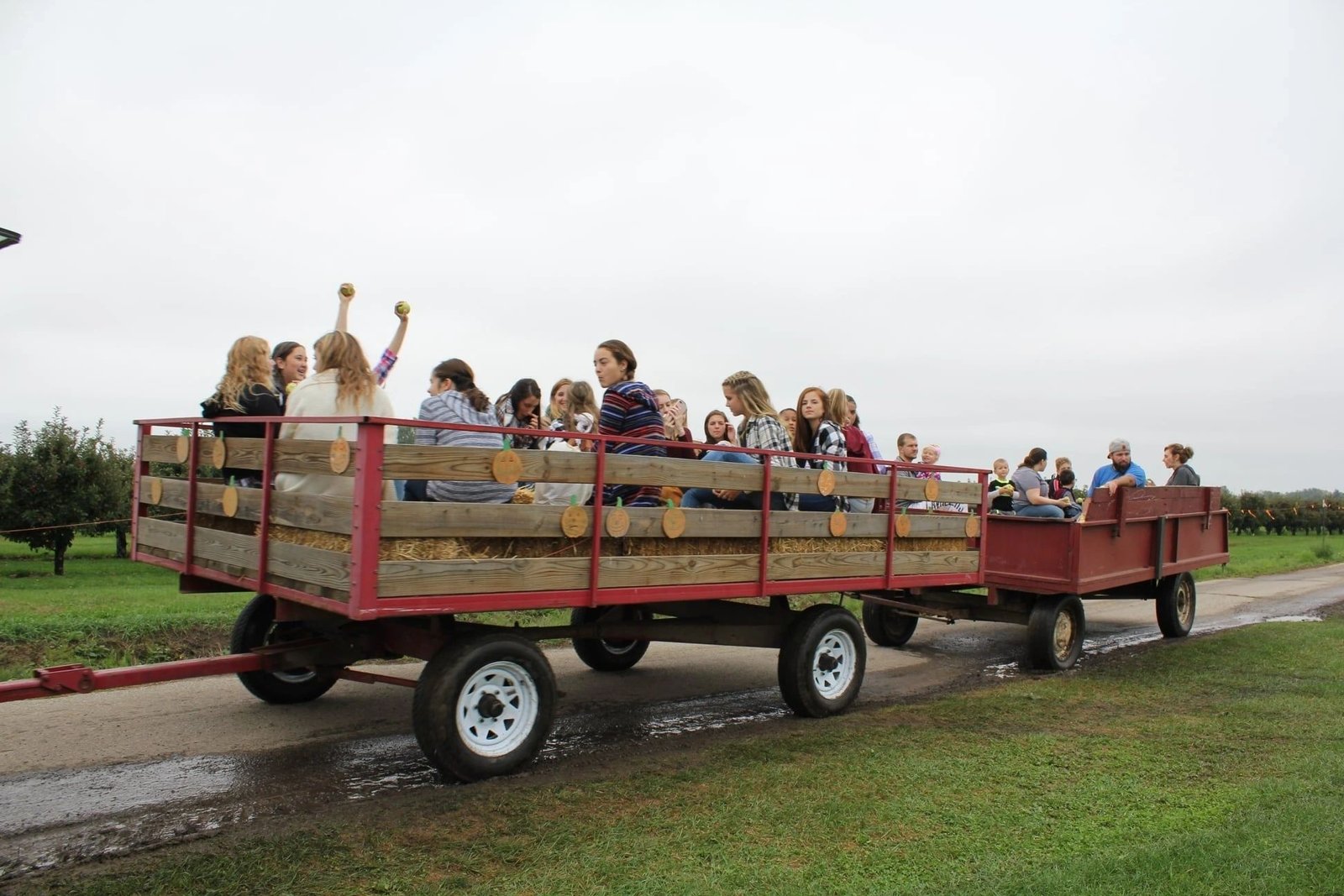 A hay wagon full of riders by the orchard