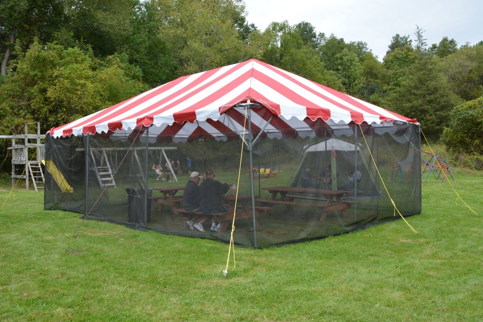 The red-and-white striped screened tent with picnic tables on the lawn