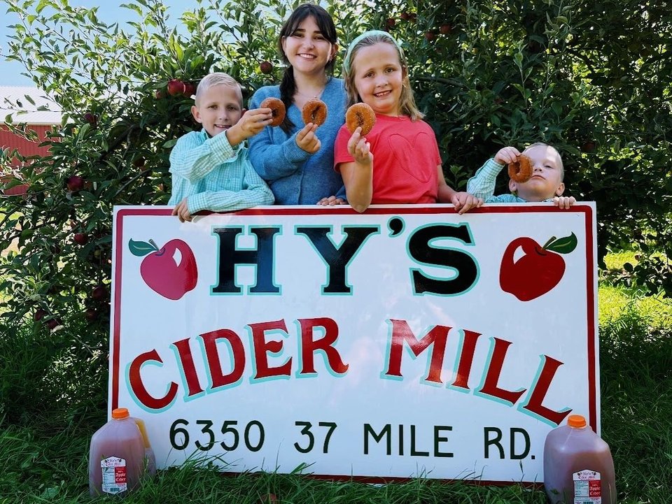 Kids with donuts behind the Hy's Cider Mill sign in the orchard