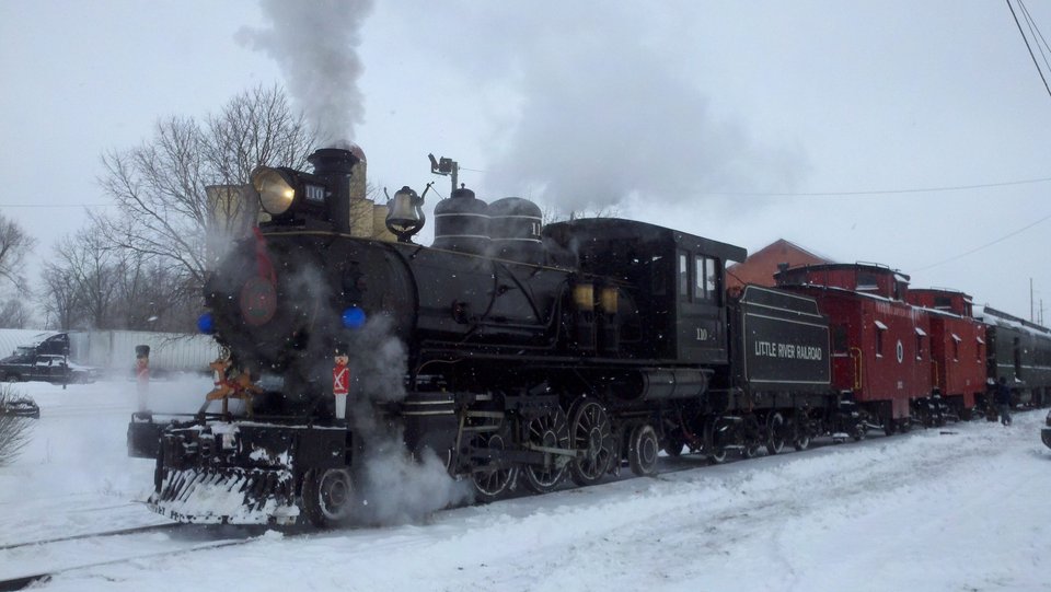 Decorated No. 110 and red cabooses in falling snow on a Christmas run