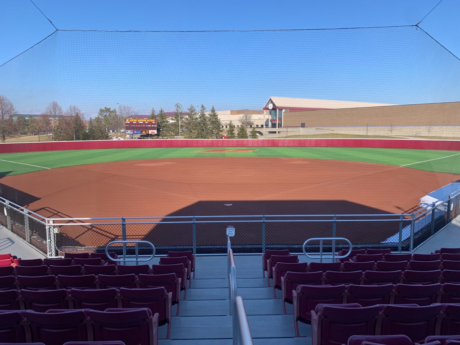 Maroon chairback seats behind home plate overlooking the softball diamond