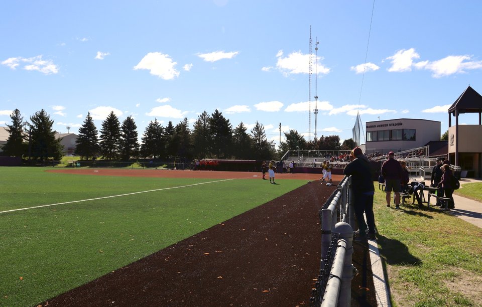 Fans along the fence during a game, the field and pines behind them