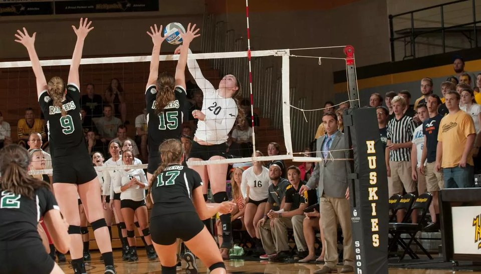 Volleyball action at the net with Huskies fans in the bleachers behind