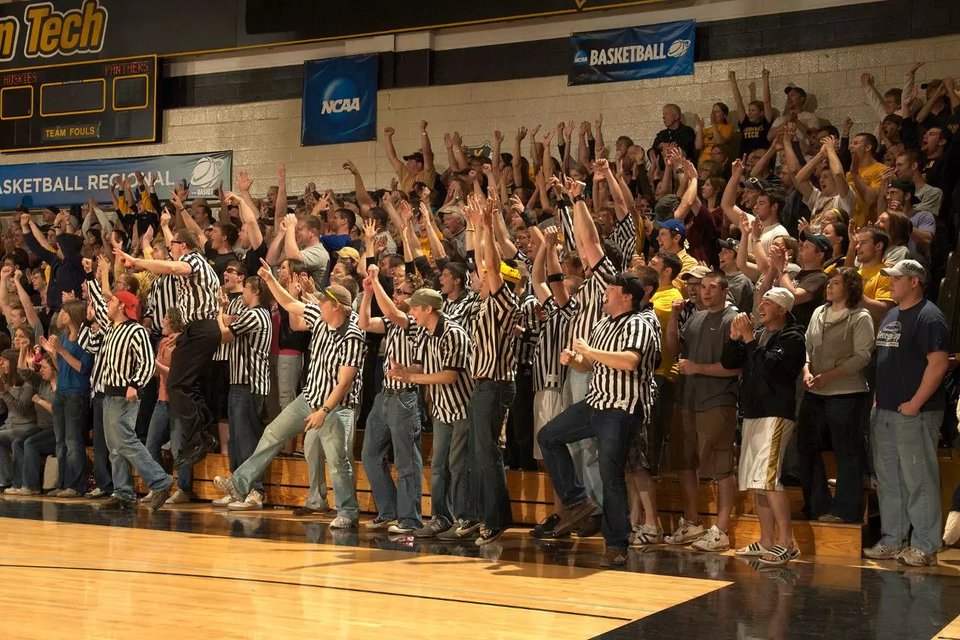 Student fans in referee stripes cheering in the bleachers