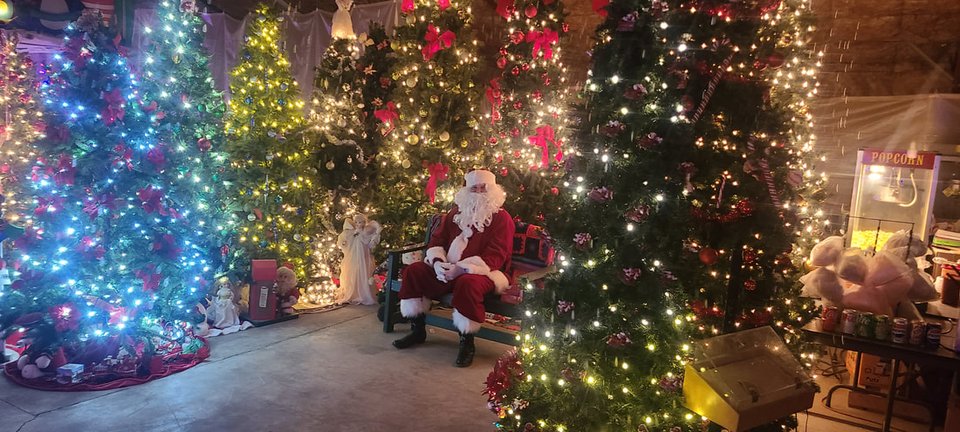A Mikulás egy padon ül a kivilágított karácsonyfák között a North Pole Express idején (2023)