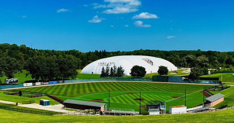 Oakland Baseball Field's striped grass seen from the spectator hill, with the university's white sports dome behind