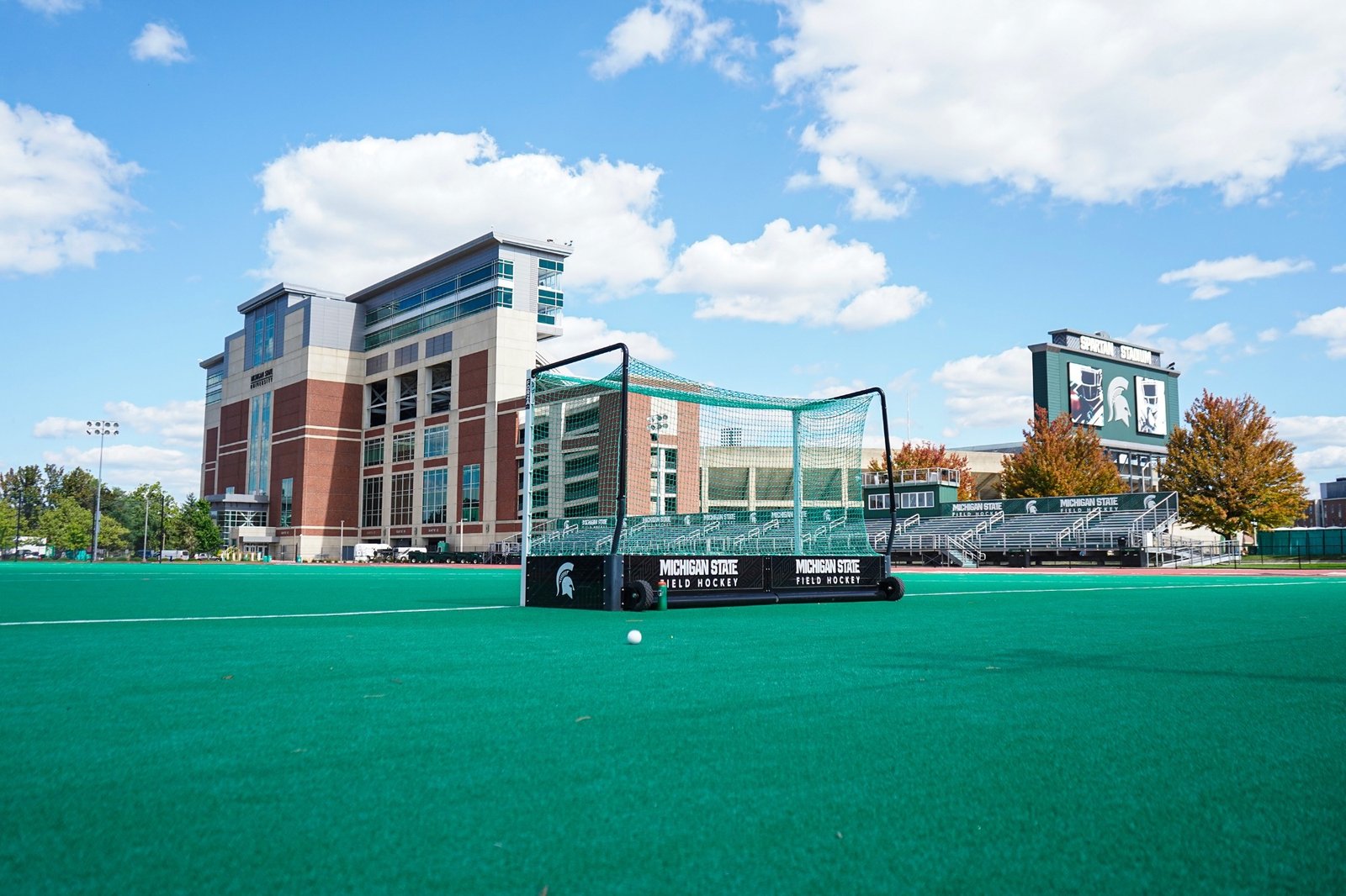 A field hockey goal on the blue-green turf with Spartan Stadium in the background