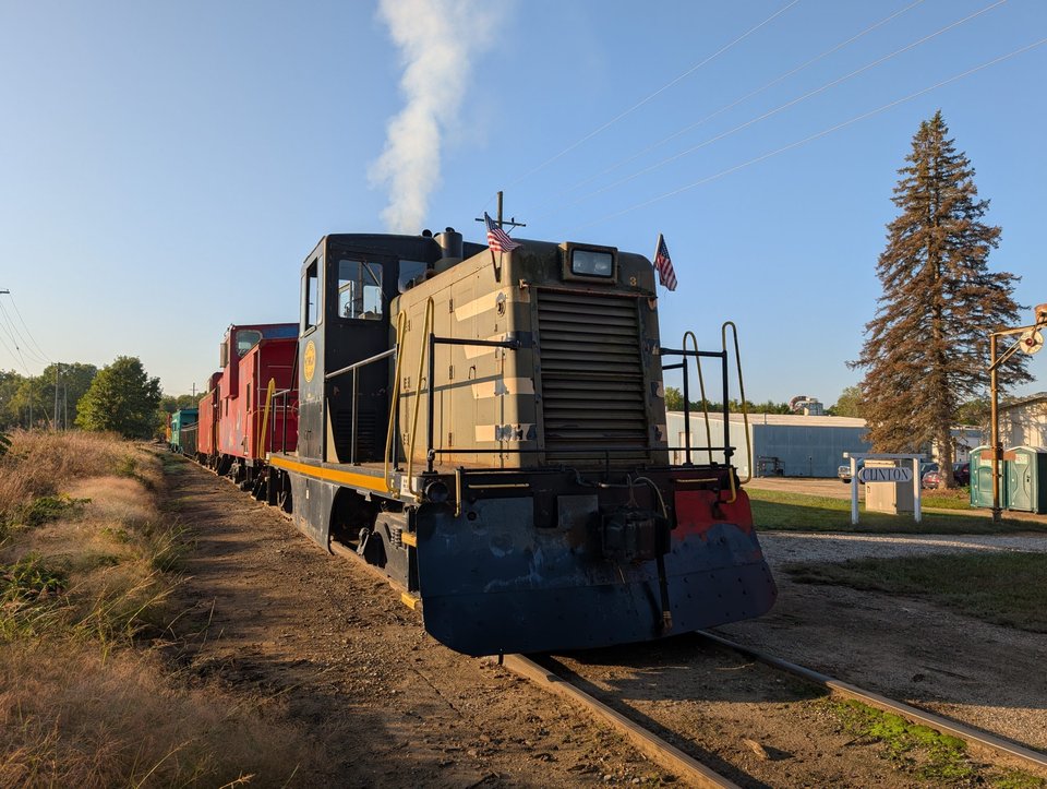 A diesel switcher and colorful cabooses beside the Clinton station sign