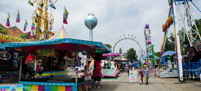 Midway booths, flags and rides at the Oakland County Fair with a water tower behind