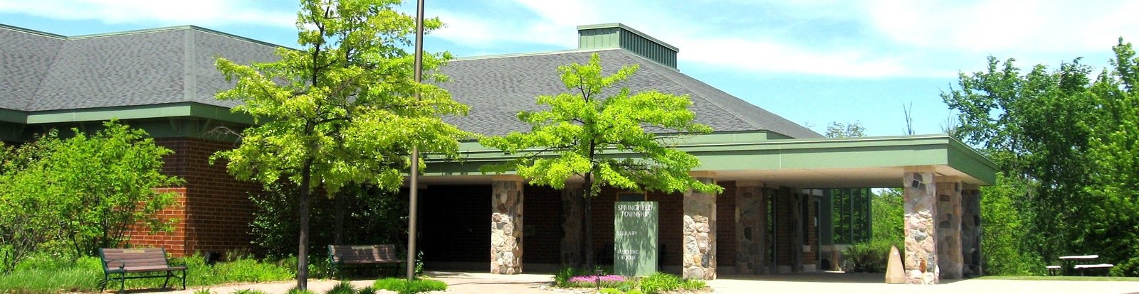 Springfield Township Library's stone-pillared entrance under a green roof, with trees and benches