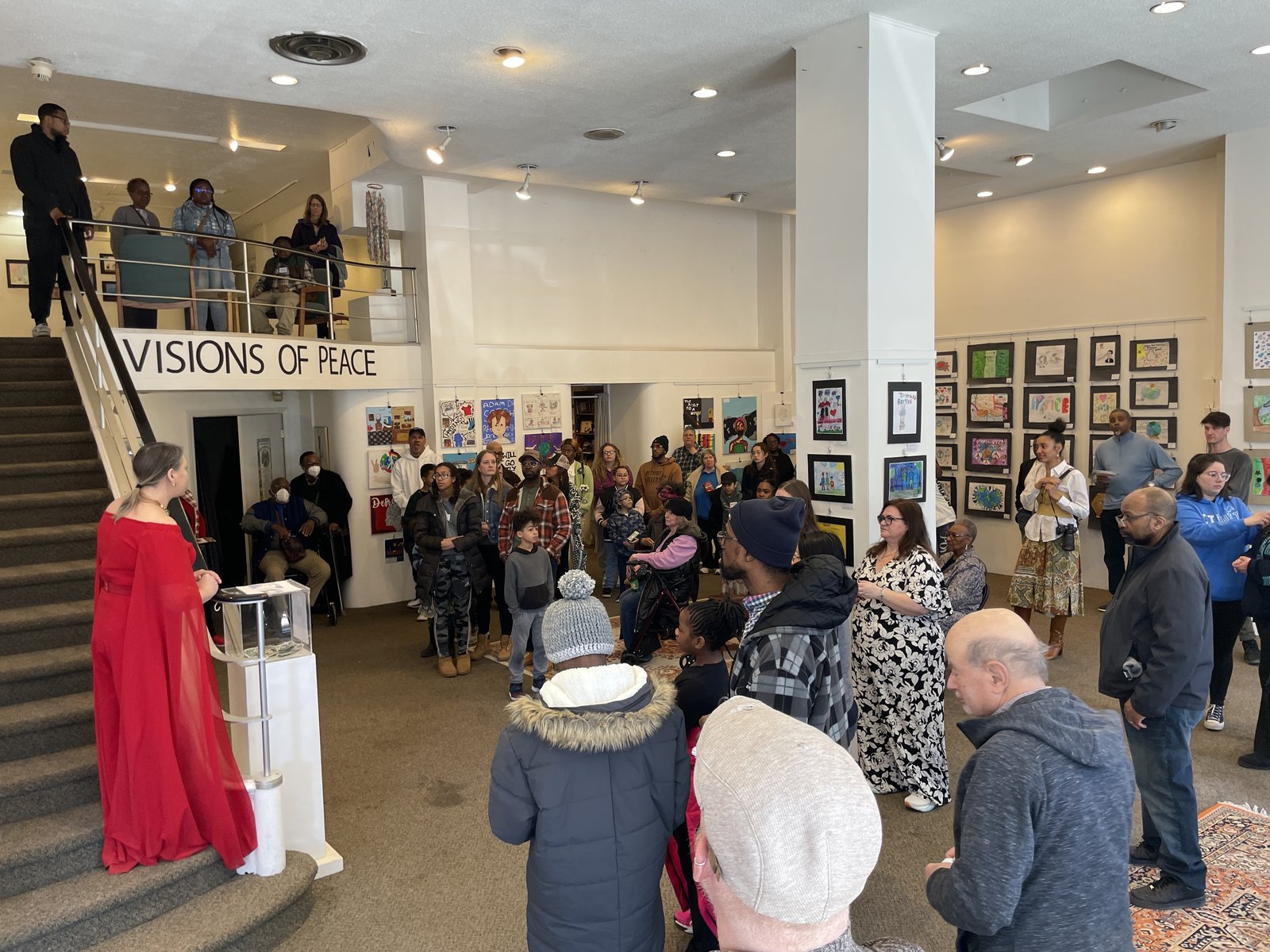An opening at the gallery, with a crowd below the stairs and the Visions of Peace mezzanine