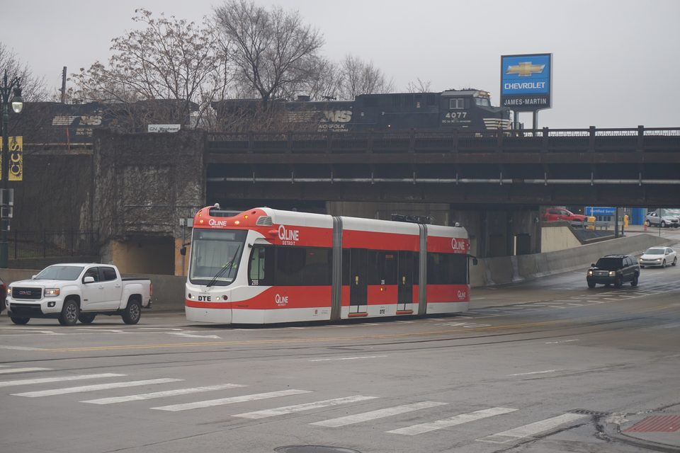 A streetcar beneath the railway bridge as a Norfolk Southern freight passes above (2021)