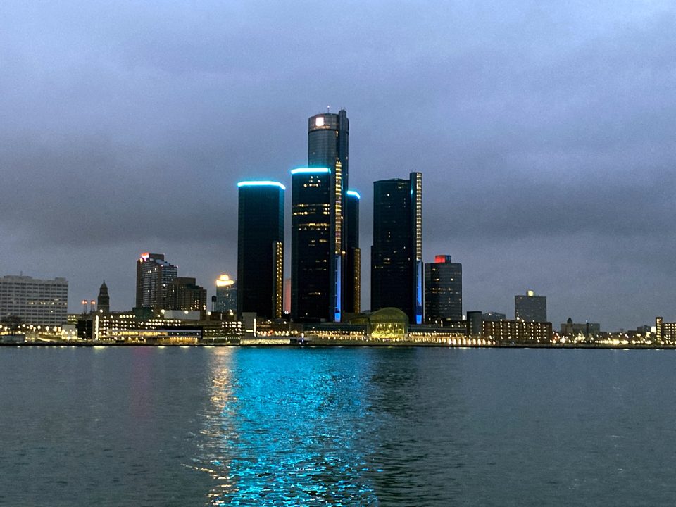 Blue-lit towers and their reflection on the water: the Renaissance Center from Windsor at dusk on December 31, 2023