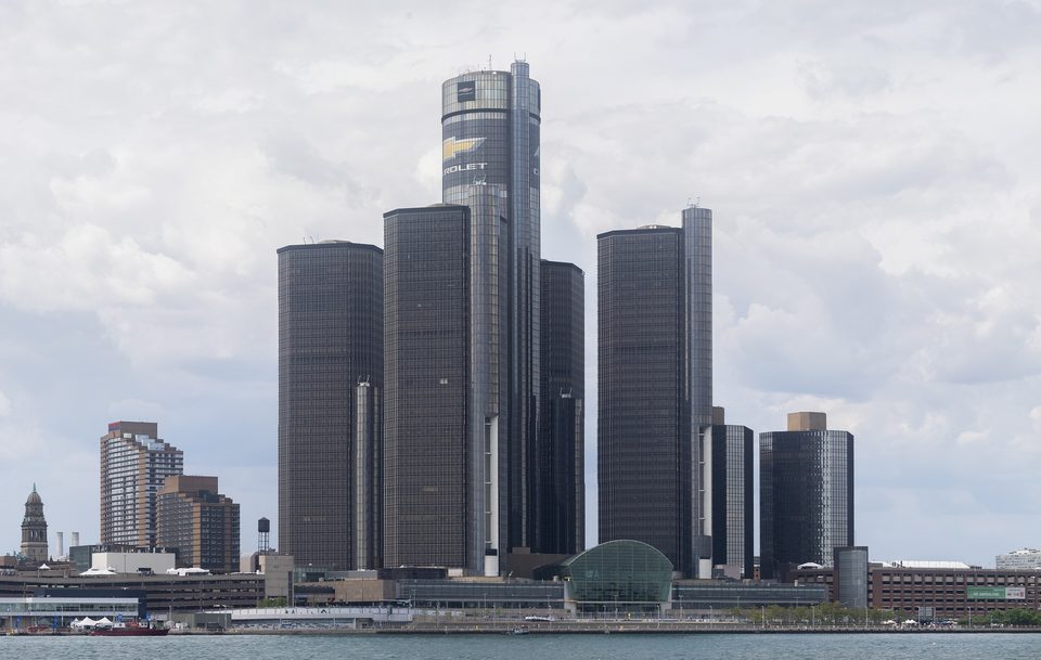 The Renaissance Center from Windsor, across the Detroit River, May 2025: the 73-story hotel cylinder in the middle, the 39-story office towers around it and the glass-vaulted Wintergarden on the water